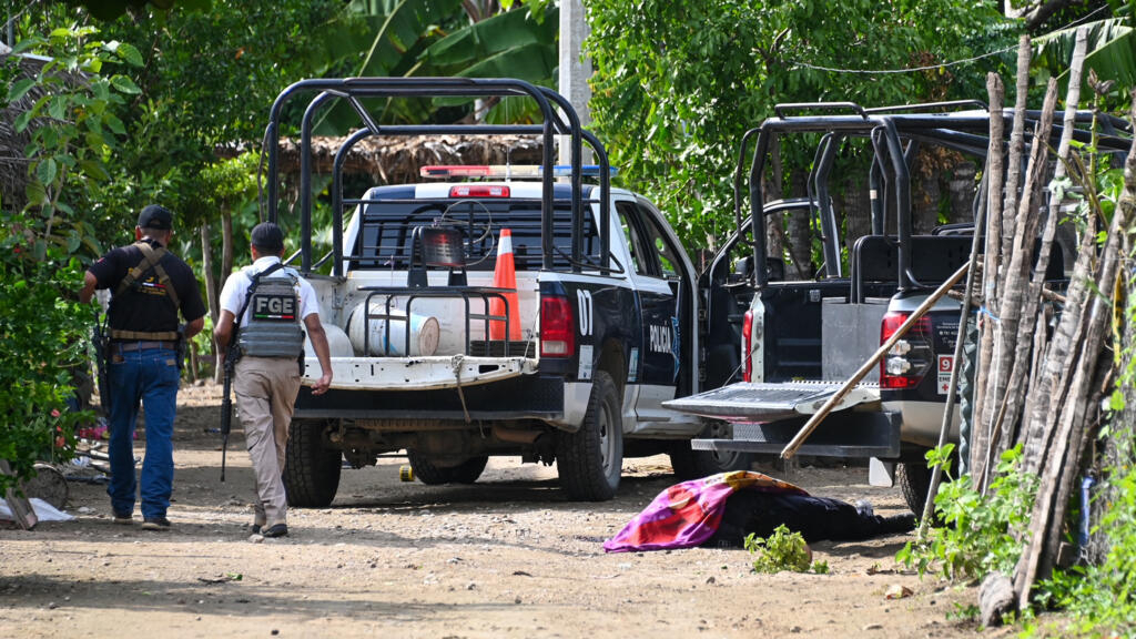 Fuerzas de seguridad pasan junto a un cadáver mientras inspeccionan la zona donde al menos 11 policías murieron en una emboscada de grupos criminales en Coyuca de Benítez, estado de Guerrero, México, el 23 de octubre de 2023